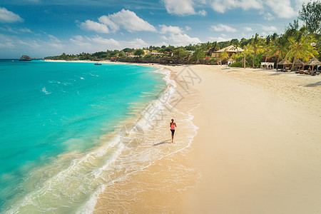 阳光明媚的日子里,海边的白色沙滩上,位正奔跑的轻女子的鸟瞰暑假顶级景观的运动苗条女孩,清澈的蔚蓝水印度洋图片