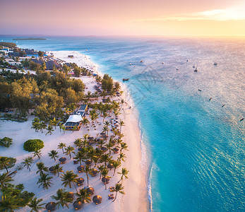 日落时,太阳伞棕榈树海边的沙滩上鸟瞰非洲桑给巴尔的夏季旅行热带景观棕榈树,船只,游艇,碧水,橙色天空空中俯瞰背景图片