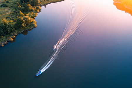 夏季日落时蓝色水中浮水滑板车的鸟瞰图乡下度假河里运动的船只的顶部视图景观与移动摩托艇绿树极端日落时碧背景图片