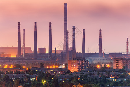 城市建筑背景上的钢铁工厂与烟囱夜间烟囱的冶金厂钢铁厂,钢铁厂重工业空气污染,烟雾工业景观背景图片