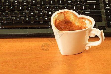 心形杯咖啡旁边的笔记本电脑键盘办公室办公桌电脑键盘旁边的杯咖啡图片