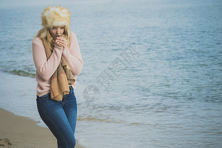 女人穿着温暖时尚的秋装,戴着毛茸茸的大帽子,但感觉很冷女海滩上放松散步时发冷穿着时尚服装的女海边感觉很冷背景图片