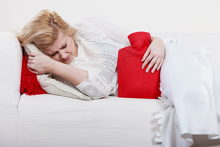 疼痛期月经痉挛问题的胃抽筋的女人躺沙发上,感觉很舒服,着热水瓶,感觉些缓解女人感觉胃抽筋躺沙发上背景图片