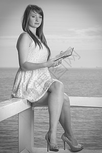 书籍,书虫,旅游,休闲时间的美丽的女人穿着白色的连衣裙坐海边的木栏上看书女人坐海边的栏上,看书图片