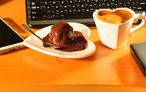杯咖啡巧克力蛋糕心形盘子碟旁边的笔记本电脑键盘智能手机办公室办公桌电脑旁边的杯咖啡巧克力蛋糕图片