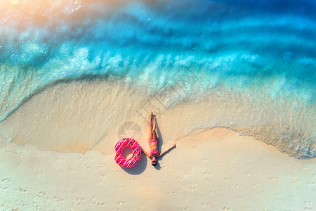 鸟瞰美丽的轻躺着的女人,粉红色的甜甜圈游泳环白色的沙滩上,靠近大海,日落时波浪暑假苗条女孩的最高视野,清澈的蔚蓝的图片