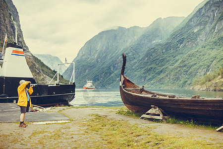 带相机的男游客挪威自然的海滨,雾蒙蒙的天,拍摄古老的木制维京船的照片山脉峡湾旅游旅游挪威的艘旧维京图片