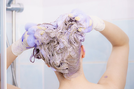 女人头发上涂上着色洗发水紫色洗涤产品的女家里涂金色女人头发上涂墨粉洗发水背景图片