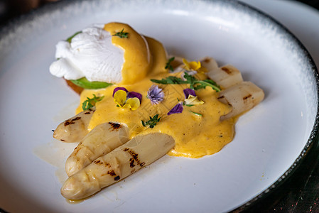美味的烤白芦笋与煮鸡蛋与荷兰风味酱装饰与食用五颜六色的花图片