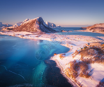 夕阳风景日落时,雪覆盖着山脉房屋清澈的水蓝天冬季景观与海岸,雪岩,罗布,道路挪威洛福滕群岛小村庄的顶部景观背景