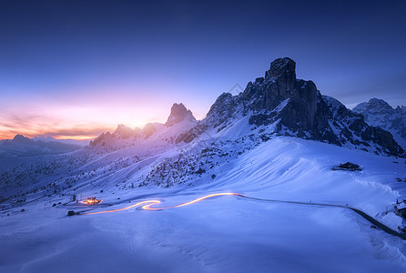 冬天,雪山模糊的汽车前灯蜿蜒的道路上美丽的景观与雪覆盖的岩石,房子,山区道路,蓝色星空日落白云石,意大利背景图片