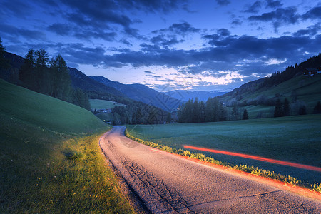 夏季夜间农村道路上模糊的汽车前灯风景与沥青道路，黄昏穿过草地的巷道图片