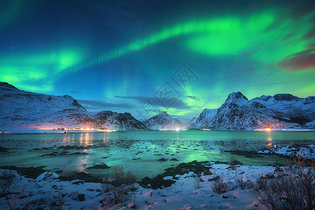 美丽星空北极光海边,雪山城市灯光夜间挪威洛福滕岛的北极光极地灯光的星空冬季景观与极光反射水中背景