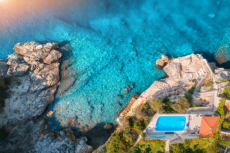 日落时,用透明的蓝色水俯瞰岩石海滩游泳池绿树大海夏季日落时亚得里亚海海岸的风景景观与蔚蓝的水,岩石豪华图片