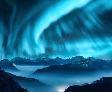冰岛极光北极光夜间雾中笼罩山上北极光天空中北极光高岩石的星星美丽的风景与极光,城市灯低云,山峰背景