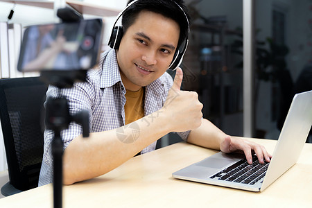 头戴式耳机轻的亚洲男玩家铸造广播他的线玩电子游戏用智能手机录制场景vlog视频关于社交媒体的线Influencerv背景