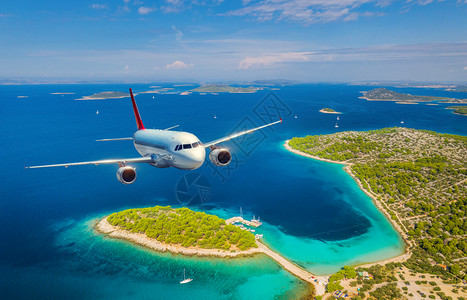 海洋小素材飞机在夏季阳光明媚的白天飞越小岛屿和海洋空中观察客机热带海岸有绿树天空和蓝水的山地背景