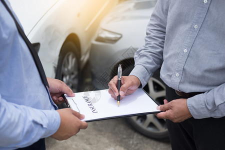 在事故后审查车辆索赔时保险代理人在剪贴板上签署保险表将笔寄给他的客户图片