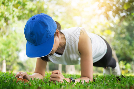 运动女穿着运动服的自信肌肉女青年在户外公园锻炼时穿戴手表练习平板支撑背景