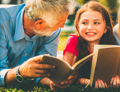 小女孩和父亲在公园草地趴着阅读书籍背景图片