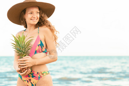 夏天在热带沙滩上穿泳衣的快年轻女子双手捧着菠萝图片