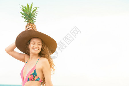 夏天在沙滩上穿泳衣的年轻女子手持菠萝在头上图片
