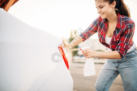 夏日可爱的女子在户外用海绵和喷雾洗车图片