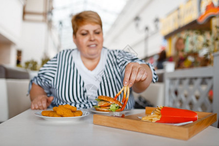 在商场食品法庭吃炸薯条的胖女人超重与垃圾午餐一起坐在桌上肥胖症图片