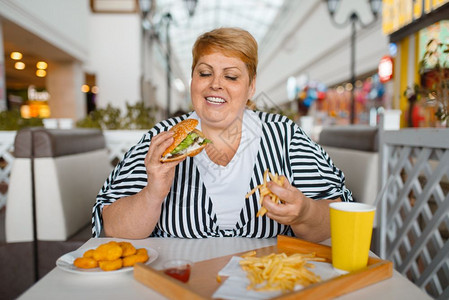 在快餐厅吃高卡路里食品的胖女人背景图片