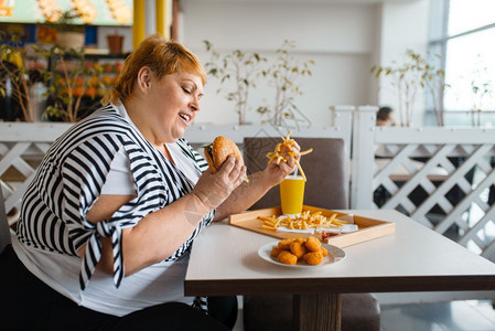 在快餐厅吃高卡路里食品的胖女人在餐桌上吃垃圾晚饭的超重女肥胖问题在餐厅吃高卡路里食品的胖女人图片