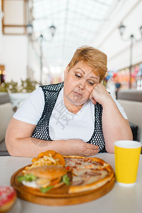 胖女人在快餐厅吃披萨不健康的食物胖女人在餐桌上吃垃圾晚饭肥胖问题女人在快餐厅吃披萨背景图片