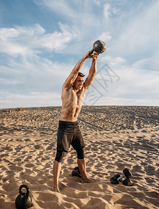 在沙漠上双手举着壶铃的肌肉男图片