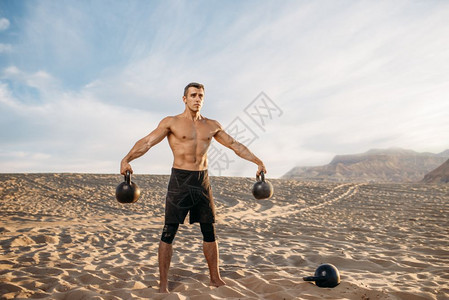 在沙漠上双手分开提着壶铃的肌肉男图片