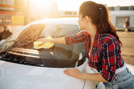 夏天年轻妇女在户外用海绵清洗车辆上的泡沫背景图片