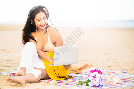 坐在沙滩上的年轻女子玩着电脑图片