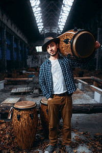 年轻的男鼓手肩上拿着木背景上是工厂的djemb音乐震荡仪器图片