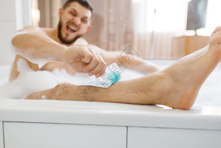 男子用泡沫早间卫生打蜡脱下腿部的毛发男子休息在浴室皮肤和身体处理程序中男子用泡沫脱下腿部的毛图片