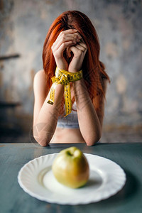 妇女双手被绑在测量胶带上用苹果脂肪或卡路里燃烧的概念来比对盘子和苹果脂肪或卡路里燃烧图片