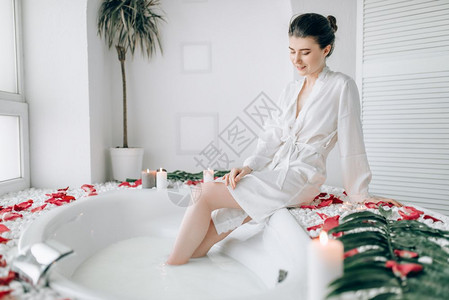 穿着白色浴袍的优雅女子坐在浴衣边上装饰着玫瑰花瓣图片