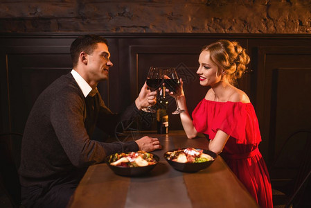 美的情侣在餐厅里举起杯子红酒在餐厅里浪漫约会穿着红礼服的优雅女人和男周年庆典图片