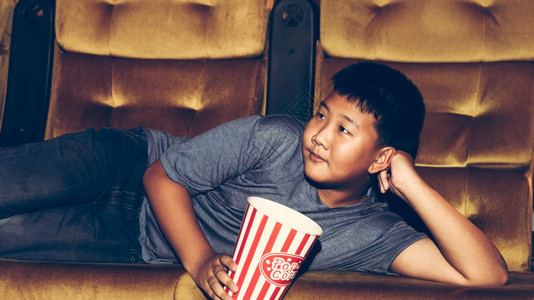 男孩躺在电影院椅子上开心地吃爆米花图片