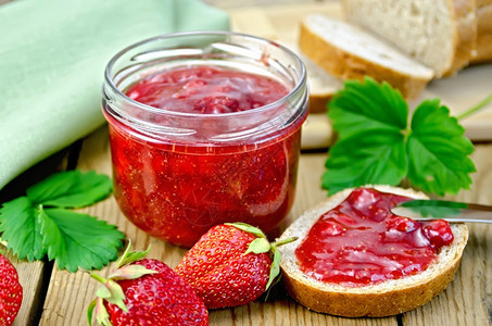 玻璃罐中草莓果酱面包草莓和叶子餐巾木板上的刀图片