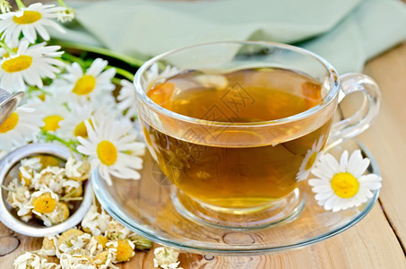 玻璃杯中的草药茶含干甘菊花的金属筛子鲜花菊木板背景上的绿布图片