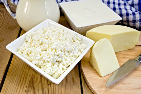 碗中的干酪和酸奶油玻璃壶中的牛奶酪刀木板上的餐巾图片
