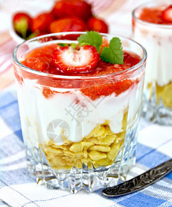 奶制品甜配有草莓玉米片和酸奶两杯汤匙蓝餐巾草莓碗里有布菜桌背景图片