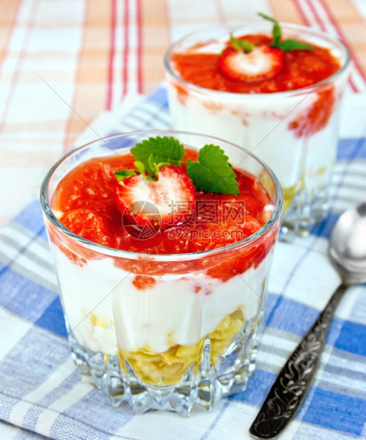 奶制品甜配有草莓玉米片和酸奶两杯勺子蓝餐巾布桌底碗中的草莓图片