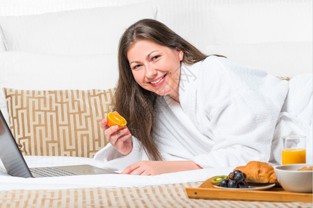 女人吃一个橙子在床上工作图片