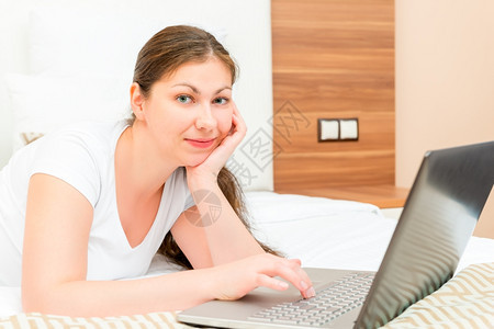 带着笔记本电脑躺在床上的年轻黑发女人背景图片