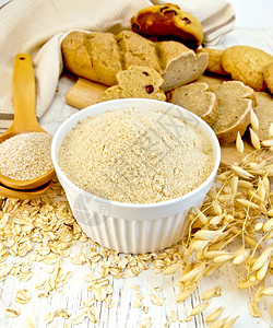 白碗中的面粉勺子燕麦和茎面包木板底的饼干图片