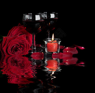 情人节日概念两杯红葡萄酒朵玫瑰和一根燃烧的红蜡烛以黑色背景隔离在小浪的水面反射图片